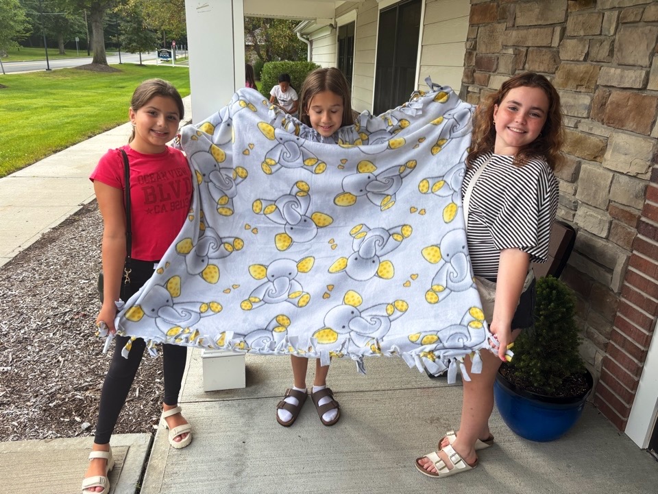 A finished yellow fleece tie blanket held by its makers