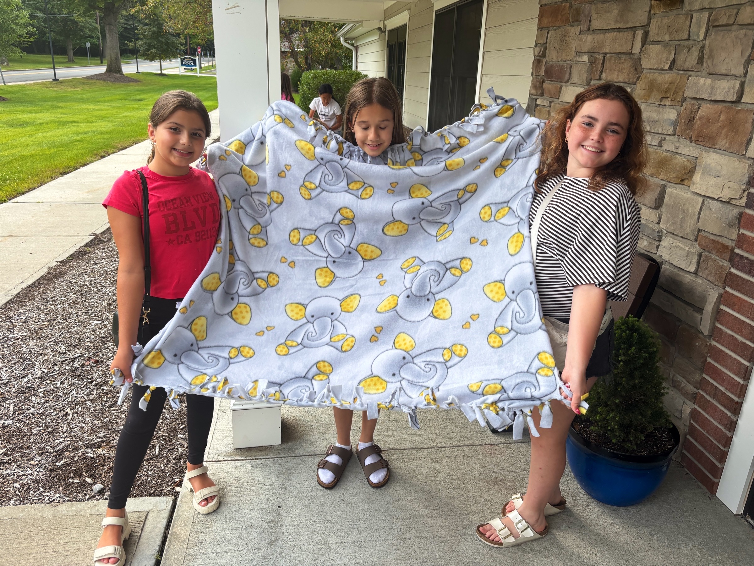 A finished yellow fleece tie blanket held by its makers